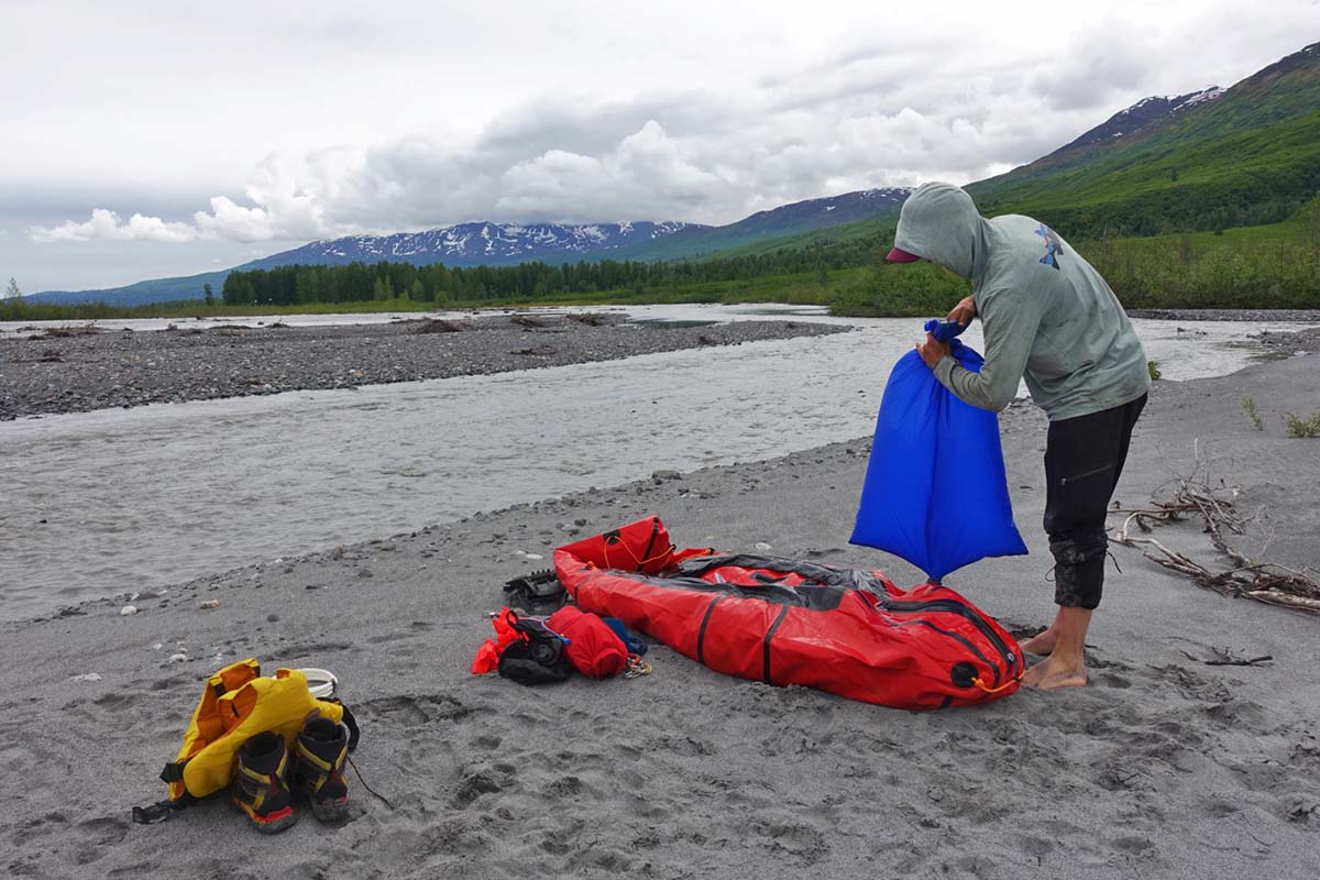 Inflating packraft beside river (inflation sack)